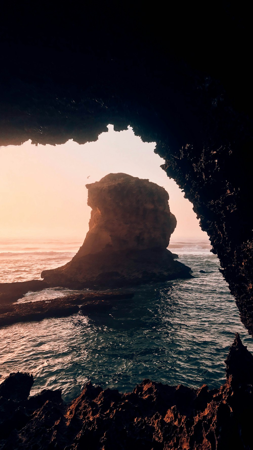 brown rock formation on body of water during sunset