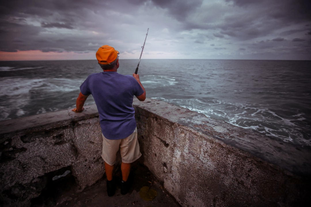 man in blue shirt and white shorts fishing on sea during daytime