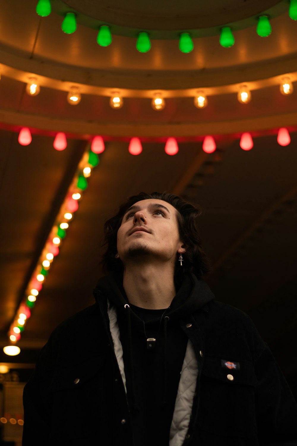 man in black jacket standing near lighted string lights
