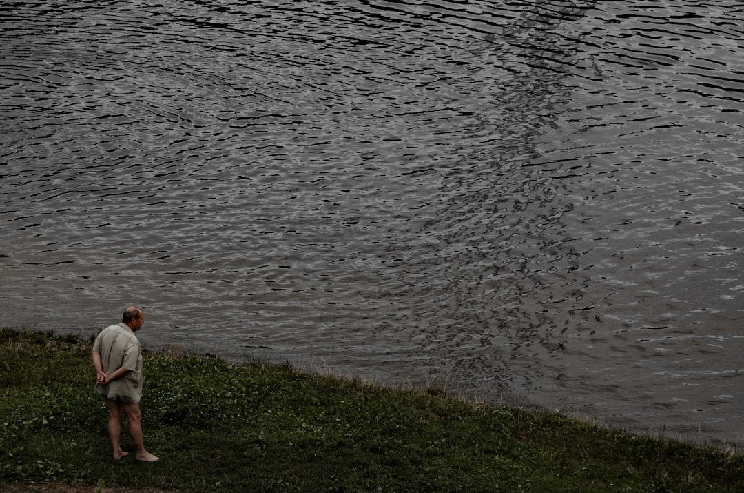 person in white long sleeve shirt standing on green grass field near body of water during