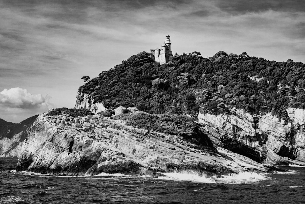 grayscale photo of lighthouse on rock formation