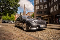 An elegant black luxury sedan showcased in front of a modern urban apartment complex under a clear blue sky.