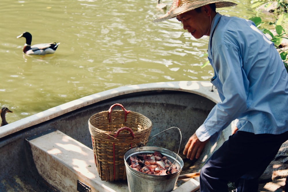 man in blue dress shirt and brown hat standing on brown wooden boat on river during