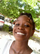 Close-up of a smiling person breathing deeply outdoors, surrounded by green trees.