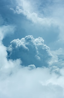 A large, fluffy cumulus cloud dominates the center, surrounded by smaller clouds against a blue sky. The lighting highlights the texture and volume of the clouds, creating a dramatic and peaceful scene.
