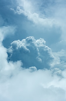 A large, fluffy cumulus cloud dominates the center, surrounded by smaller clouds against a blue sky. The lighting highlights the texture and volume of the clouds, creating a dramatic and peaceful scene.
