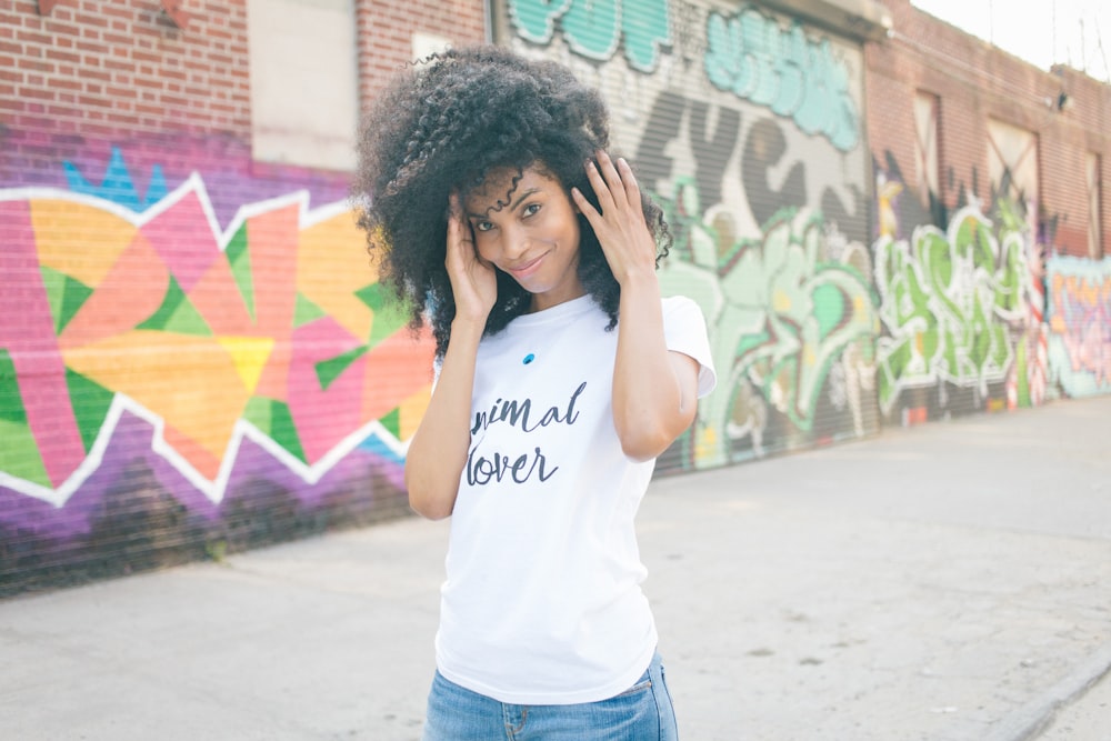 woman in white t-shirt and blue denim jeans standing near graffiti wall during daytime