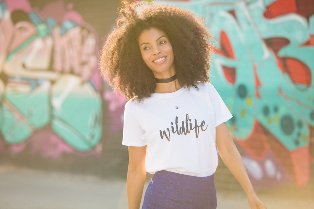 woman in white crew neck t-shirt and black skirt standing near graffiti wall during daytime