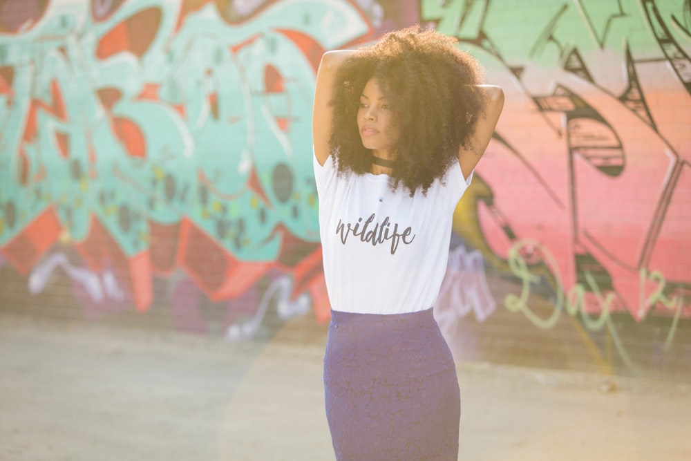 woman in white shirt and black leggings standing near wall with graffiti