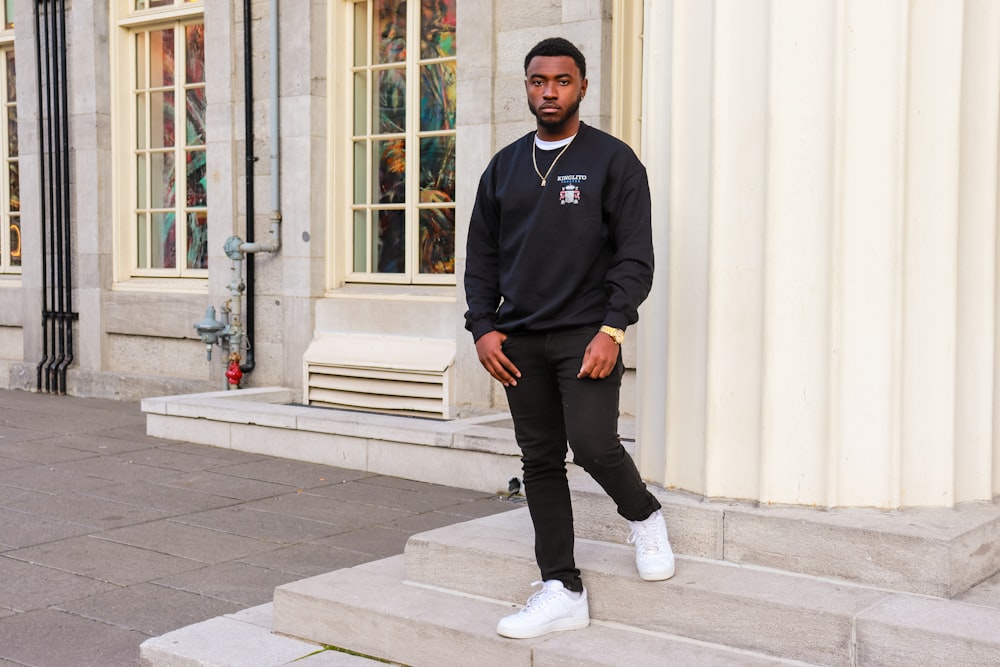 man in black sweater and black pants standing on sidewalk during daytime