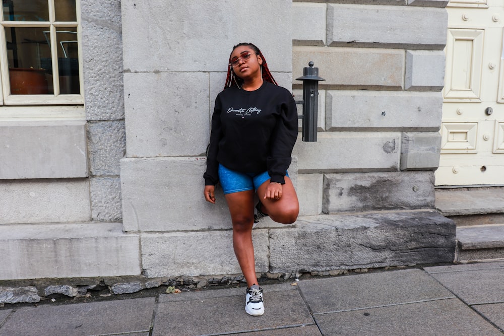 woman in black long sleeve shirt and blue denim shorts standing on gray concrete floor