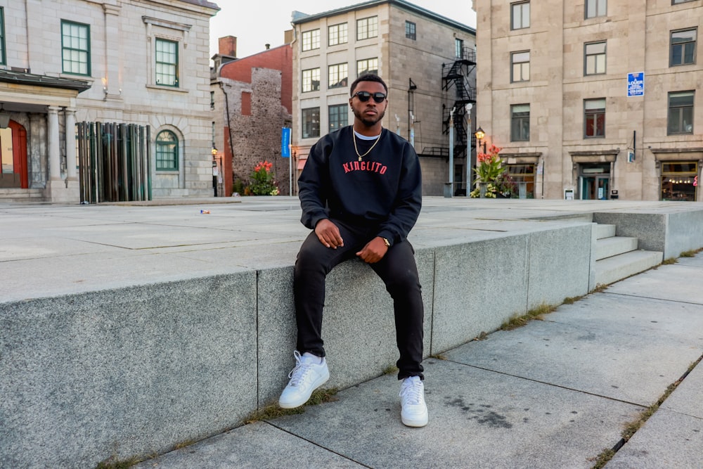 man in blue and black adidas sweater and blue denim jeans sitting on gray  concrete bench photo – Free Image on Unsplash