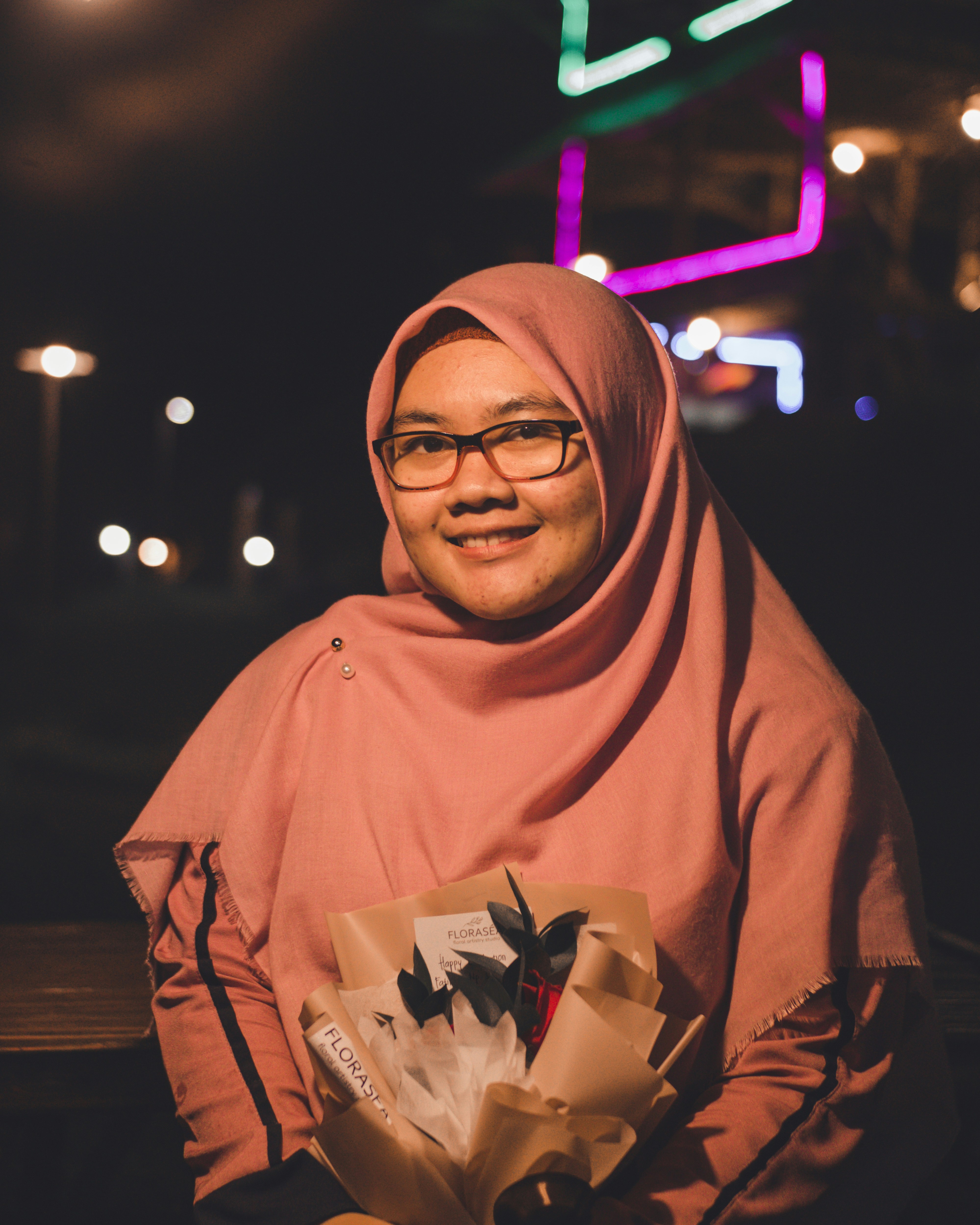 Wanita berjilbab coklat memegang hadiah putih dan coklat