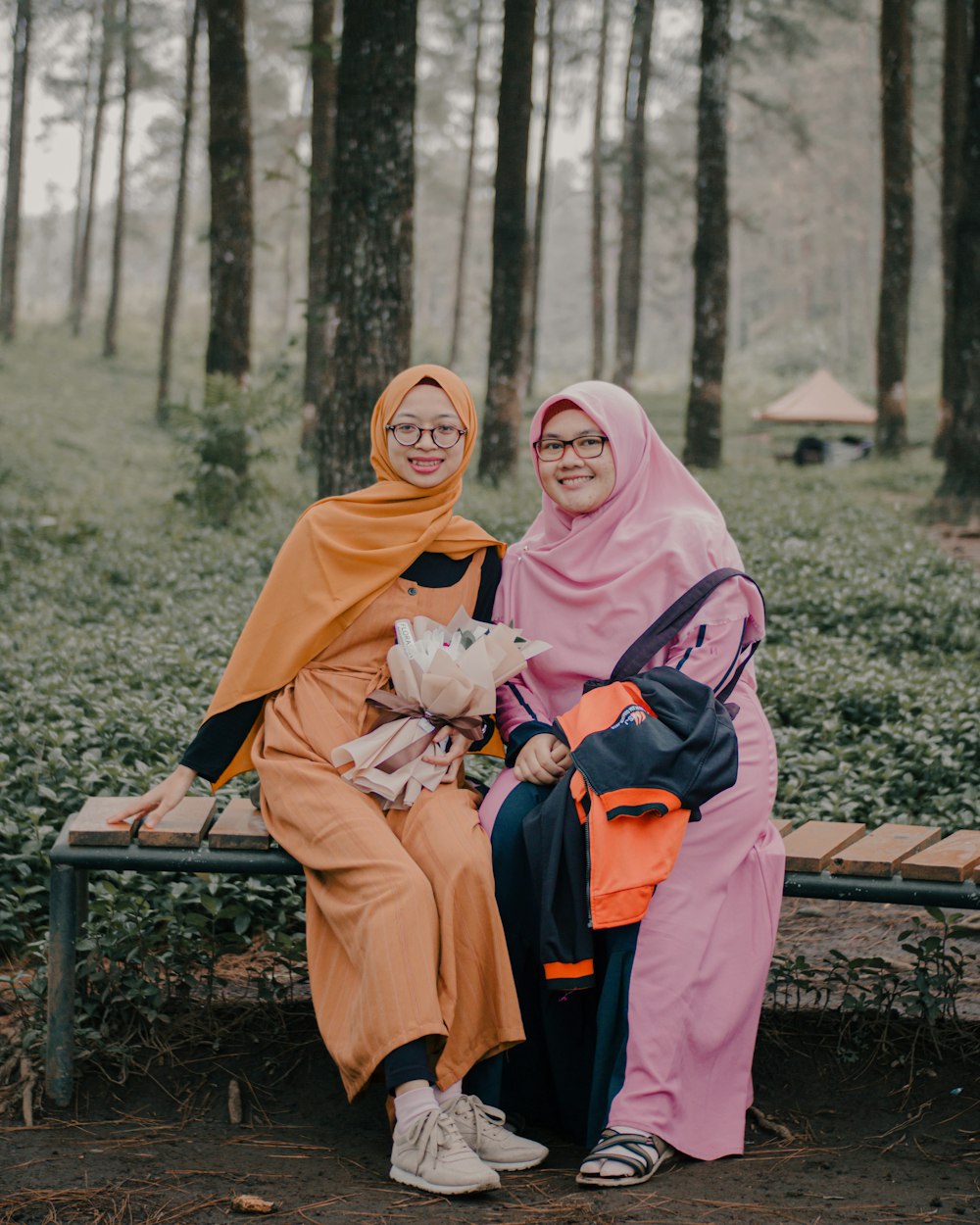 2 women in hijab sitting on brown wooden bench