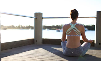 A smiling woman in écospotif sportswear holding a yoga mat, standing on a sunlit wooden deck.