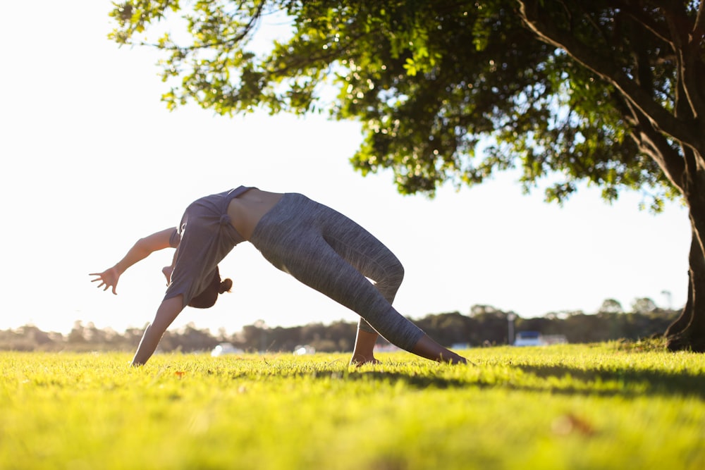 man in gray pants and white shirt jumping on green grass field during daytime