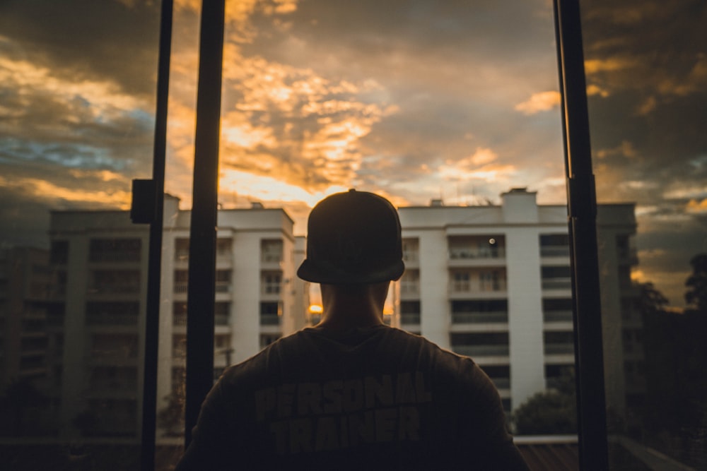 man in black knit cap and black jacket standing near window during sunset