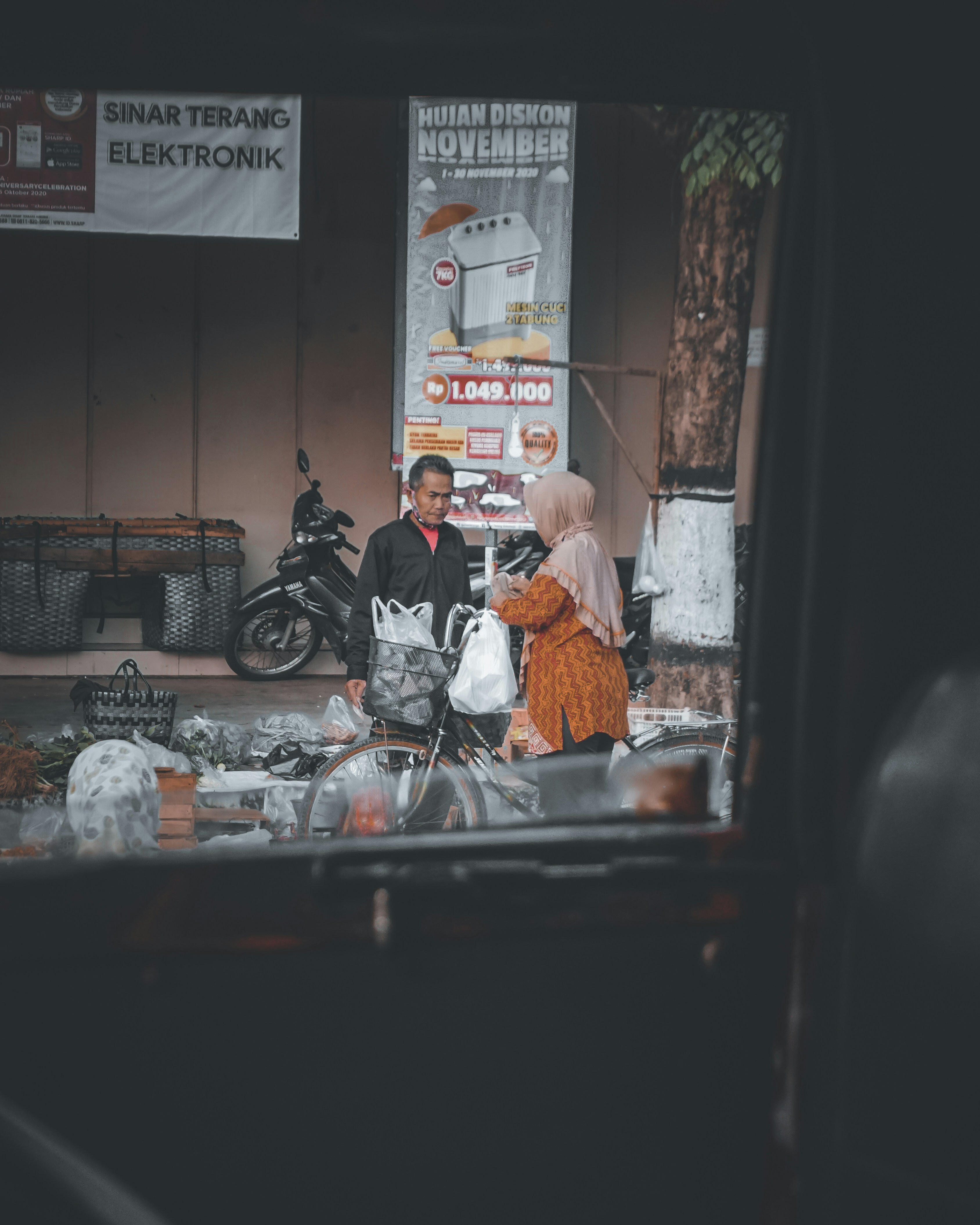 Pria berjaket hitam dan celana putih duduk di atas sepeda motor hitam di siang hari