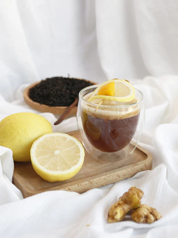 An overhead shot of a tea setup with a teapot, cups, and ingredients like green tea leaves and lemon.
