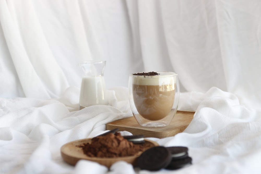 vaso transparente sobre platillo de cerámica blanca junto a galletas marrones sobre mantel blanco