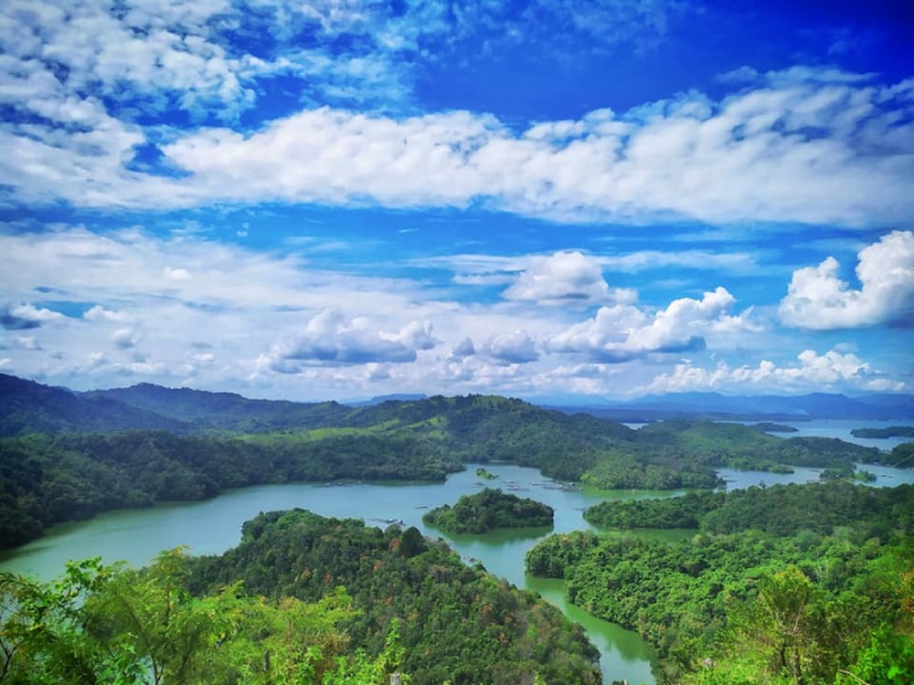 árboles verdes y montañas bajo el cielo azul y nubes blancas durante el día