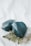 Two large, faceted dark teal crystals are placed on a light background alongside a fern leaf. The crystals have a glossy texture, and the leaf adds a natural element to the composition.