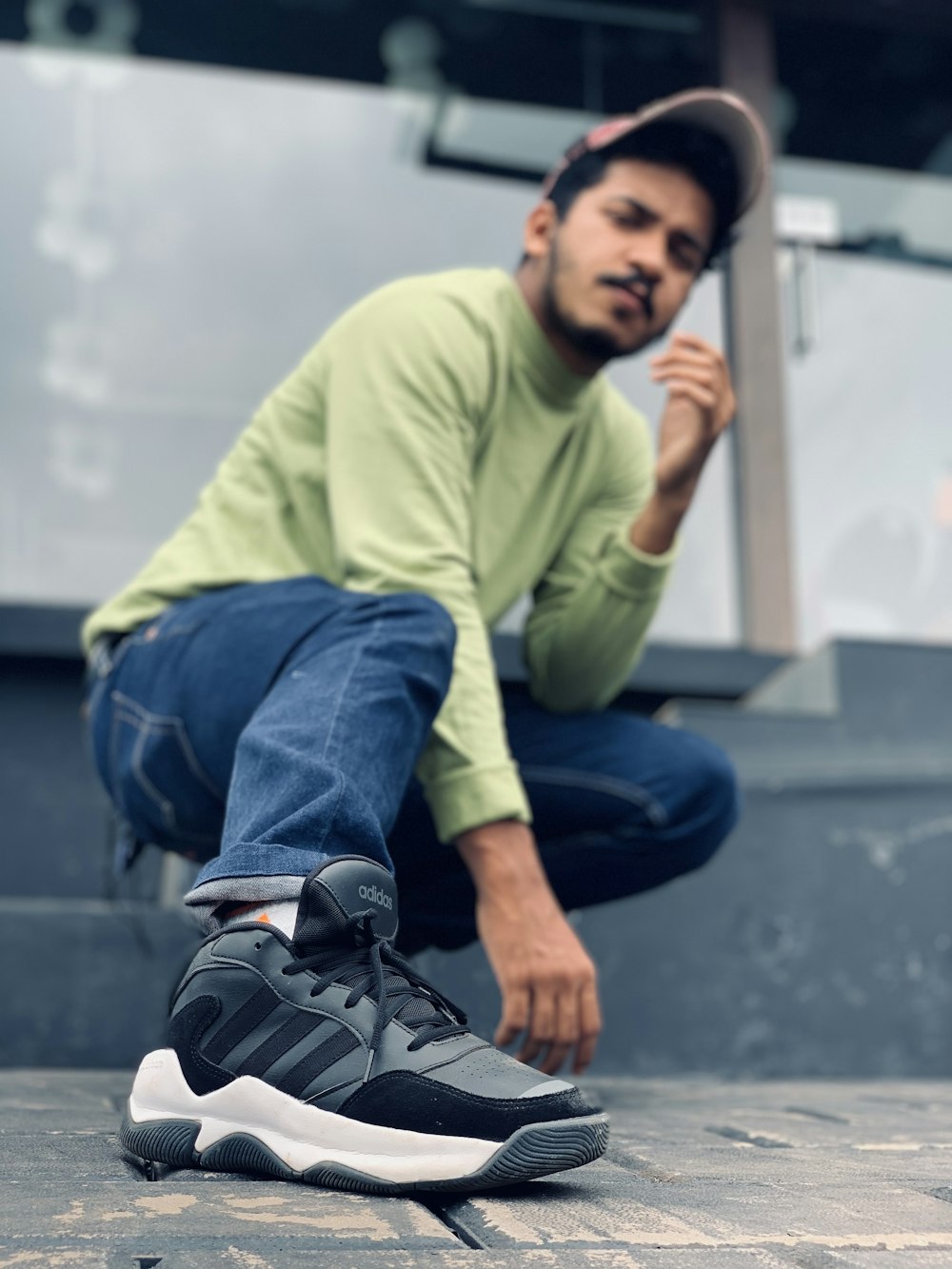 man in green sweater and blue denim jeans sitting on concrete bench