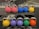 A row of colorful kettlebells arranged on a gym rack. The kettlebells are in various colors including pink, blue, yellow, purple, green, and orange. Each kettlebell has a metallic handle and is marked with a weight indication.