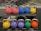 A row of colorful kettlebells arranged on a gym rack. The kettlebells are in various colors including pink, blue, yellow, purple, green, and orange. Each kettlebell has a metallic handle and is marked with a weight indication.