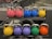 A row of colorful kettlebells arranged on a gym rack. The kettlebells are in various colors including pink, blue, yellow, purple, green, and orange. Each kettlebell has a metallic handle and is marked with a weight indication.
