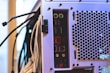 The image features the back panel of a computer tower with various ports and connectors, including USB ports, audio jacks, and PS/2 connectors, alongside a ventilation area with a hexagonal mesh design. Numerous cables are connected to the ports and extend outward.