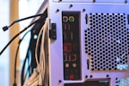 The image features the back panel of a computer tower with various ports and connectors, including USB ports, audio jacks, and PS/2 connectors, alongside a ventilation area with a hexagonal mesh design. Numerous cables are connected to the ports and extend outward.