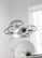 A drone hovers indoors, enclosed in a protective cage around its propellers, providing an added layer of safety. Behind it, a round mirror is visible next to a small plant, and a softly lit window allows natural light to filter into the room, creating a clean and modern aesthetic.
