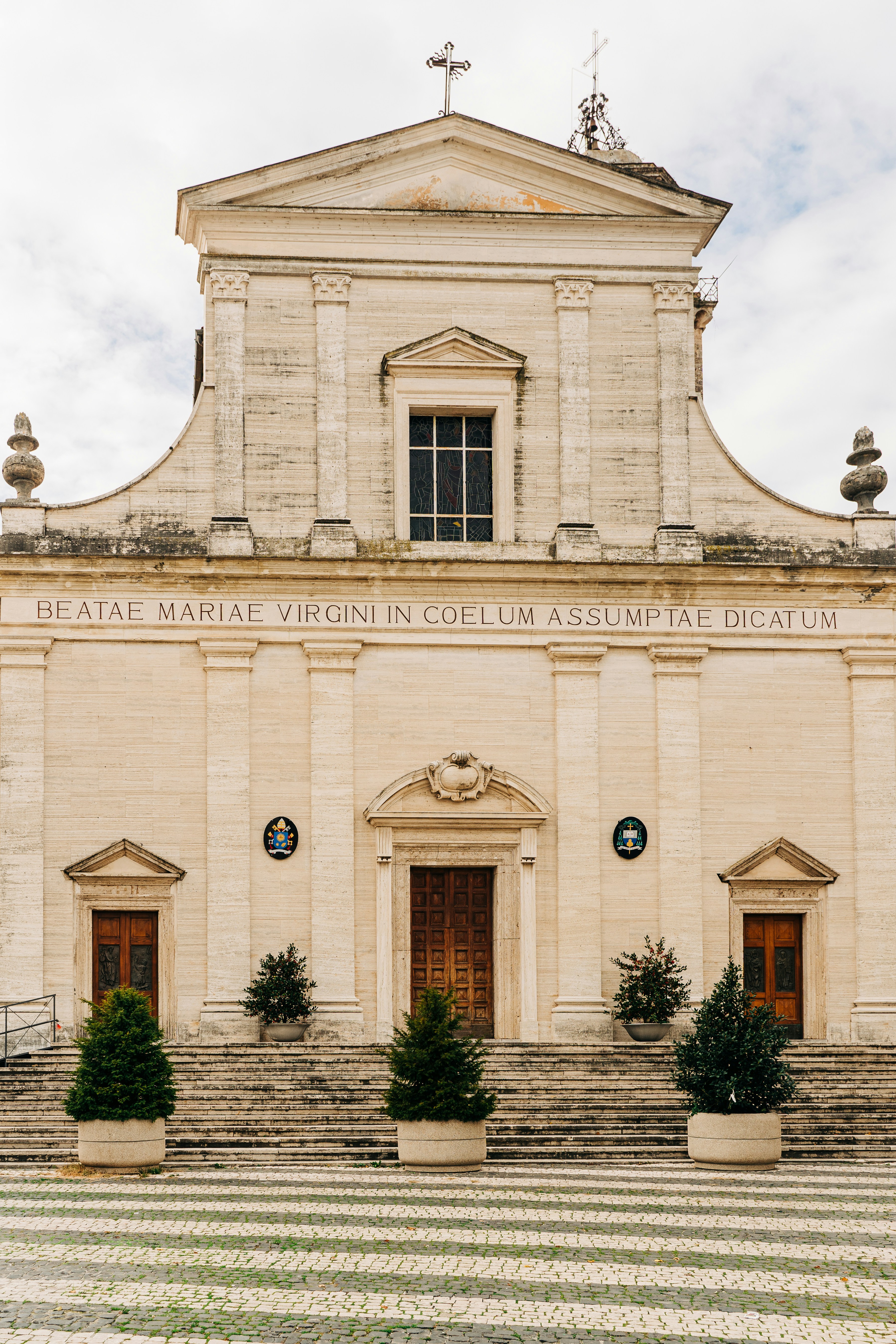Historic beige stone church facade with three doors and a cross.