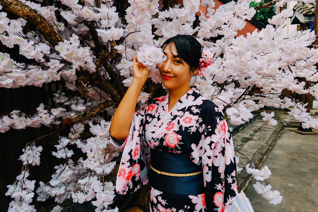 woman in black white and red floral kimono standing under white cherry blossom tree during daytime