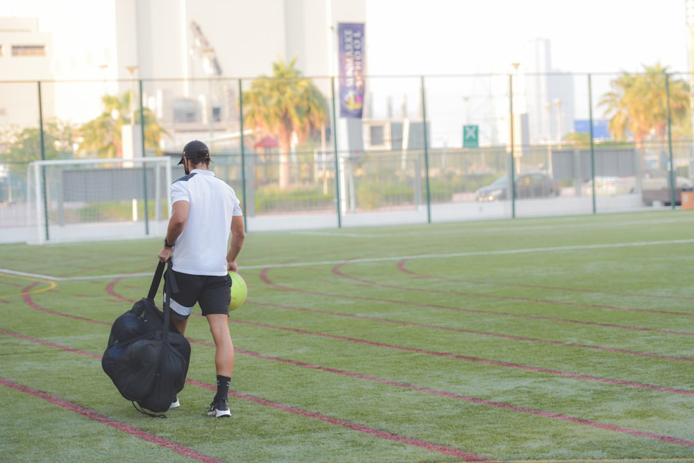 man in white t-shirt and black shorts running on green field during daytime