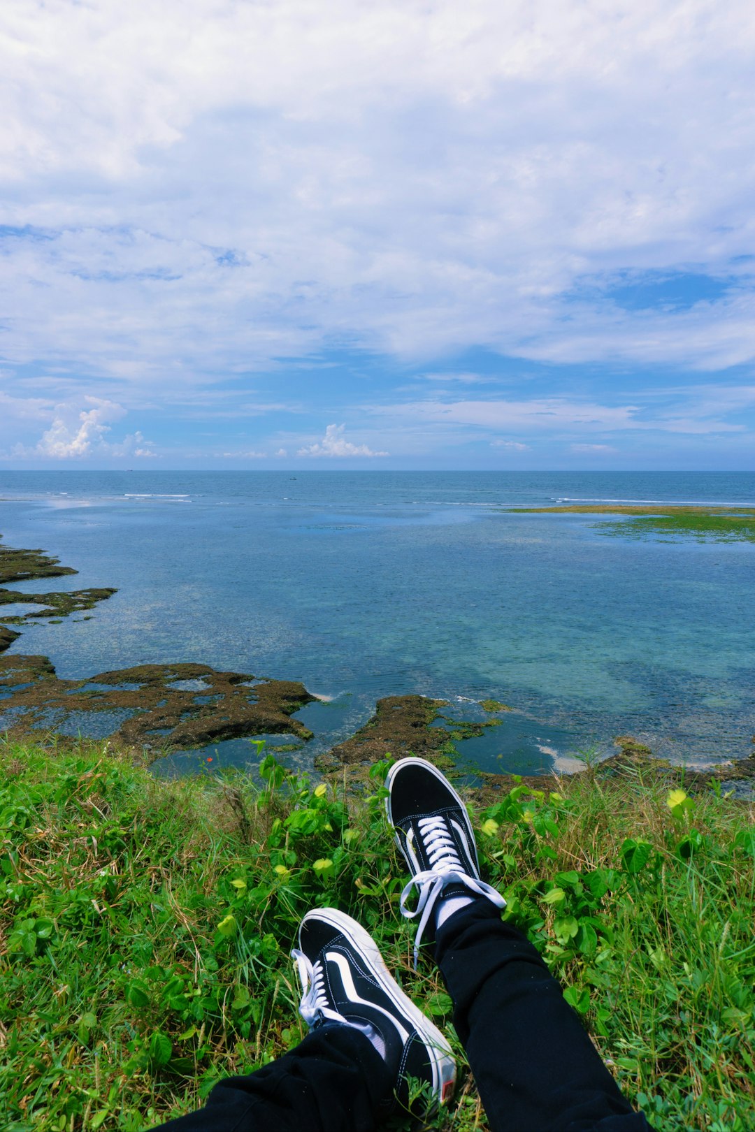 person in black and white sneakers sitting on rock by the sea under blue and white