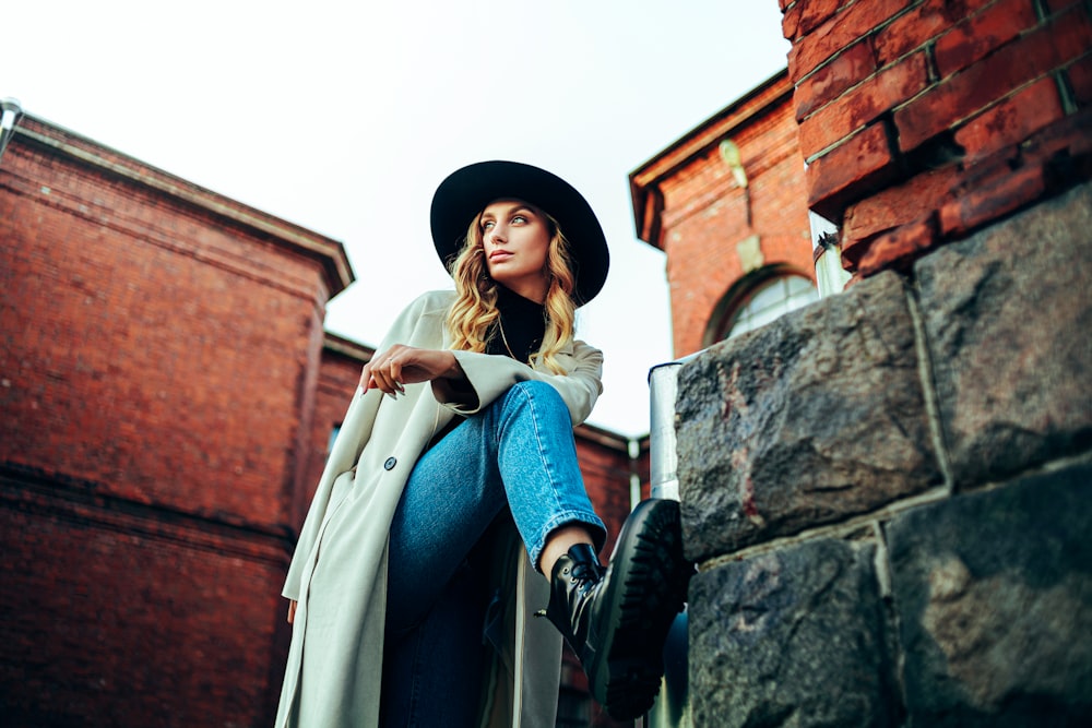 woman in blue long sleeve dress and brown coat standing beside concrete wall during daytime