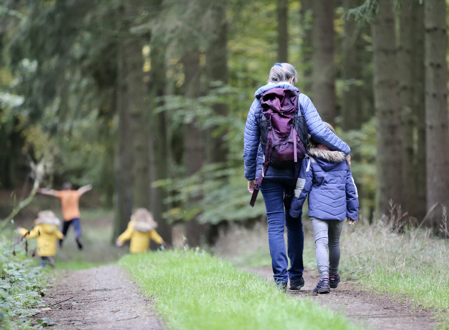 A grandmother and children walking together along a forest path.