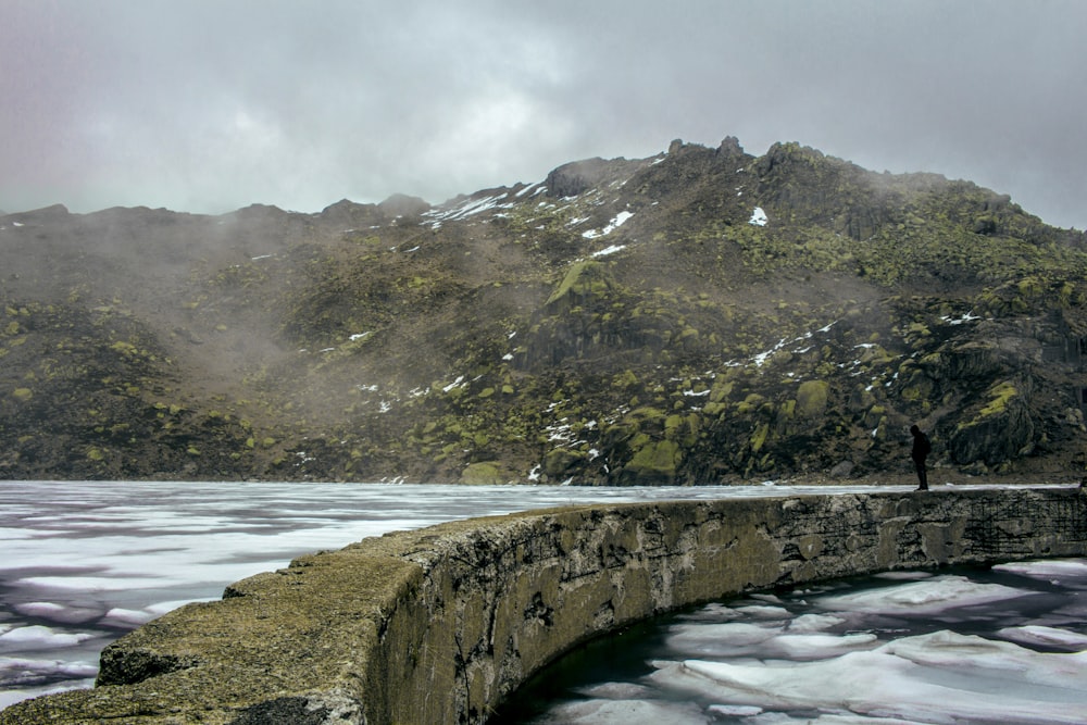 Montaña verde y gris al lado del cuerpo de agua durante el día