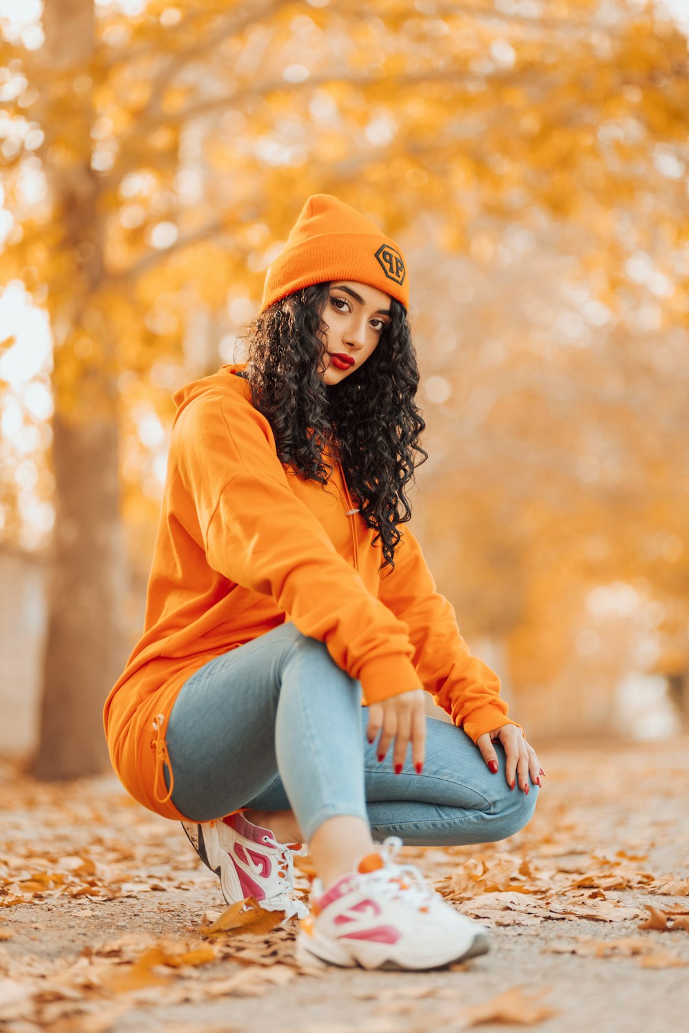 Femme en sweat à capuche orange et jean bleu assise sur le sol pendant la journée