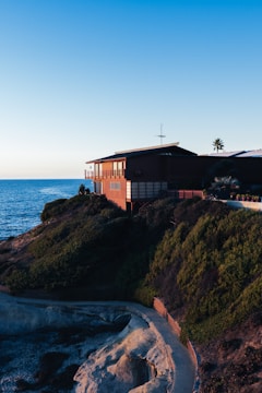 Modern steel villa perched on a cliff with panoramic ocean views under a clear blue sky.