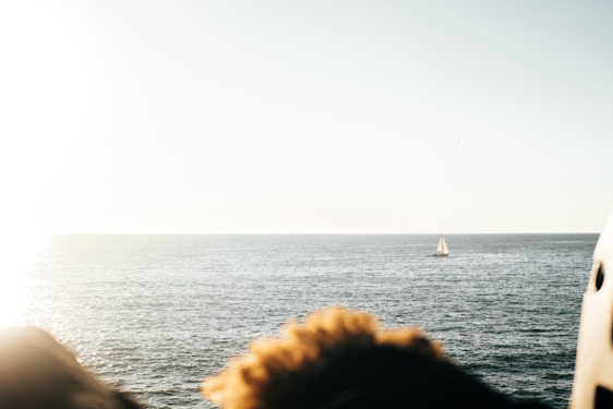 A serene turquoise ocean view with a sailboat gliding near a sunlit tropical beach.