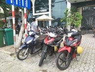 A row of motorcycles lined up outside a modern building, ready for rental.