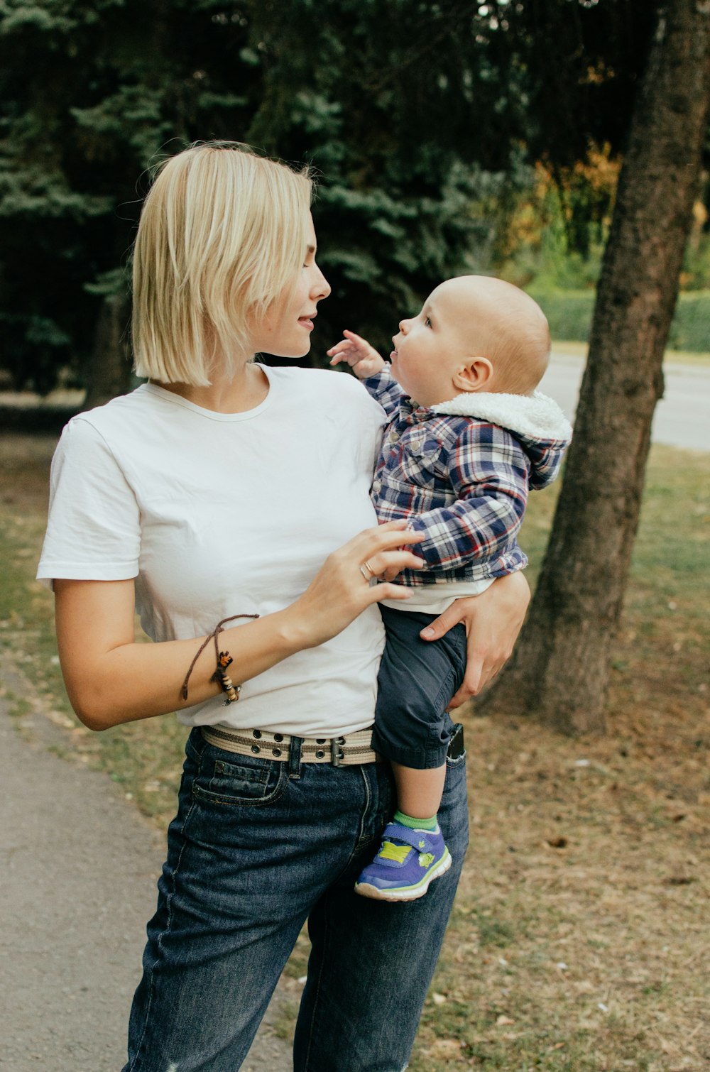 Mujer con camisa blanca que lleva al bebé con camisa a cuadros azul y blanca