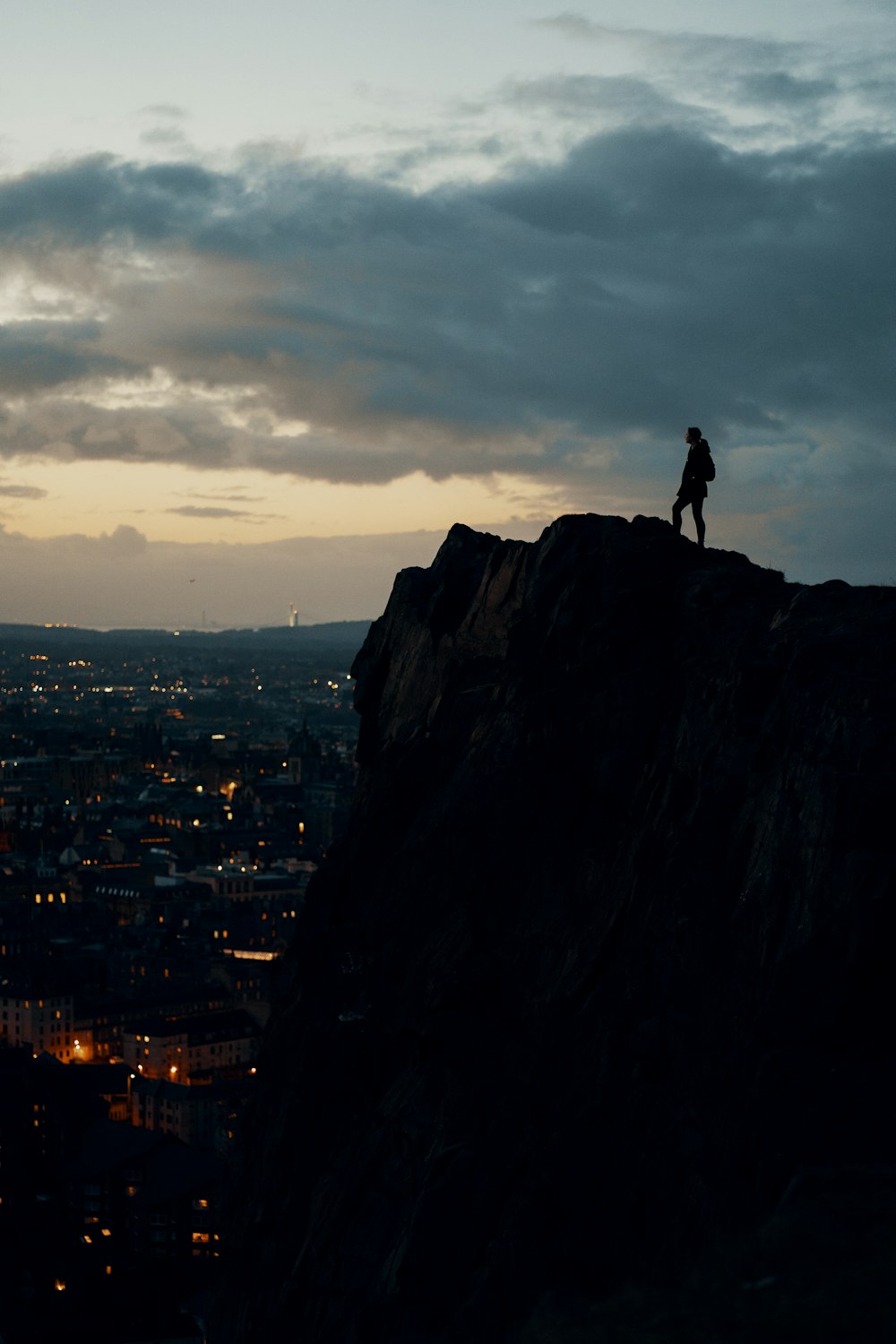 silhouette of man standing on rock formation during sunset