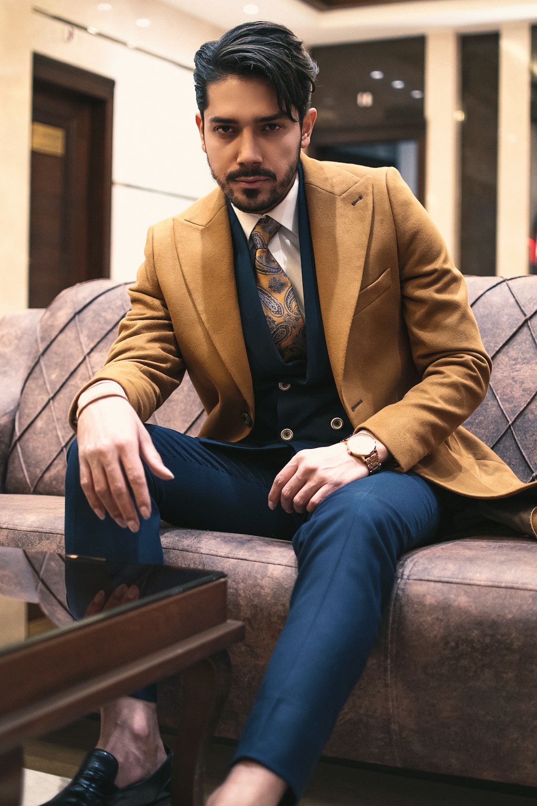 man in brown suit jacket and blue denim jeans sitting on brown wooden bench