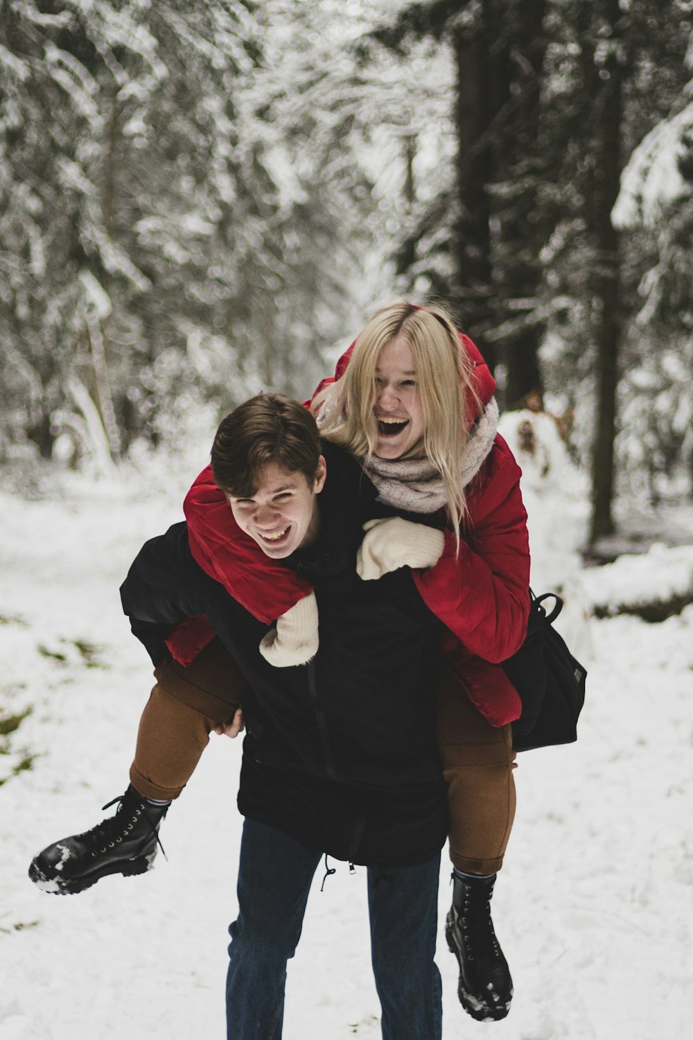 woman in black jacket carrying girl in red jacket on snow covered ground during daytime