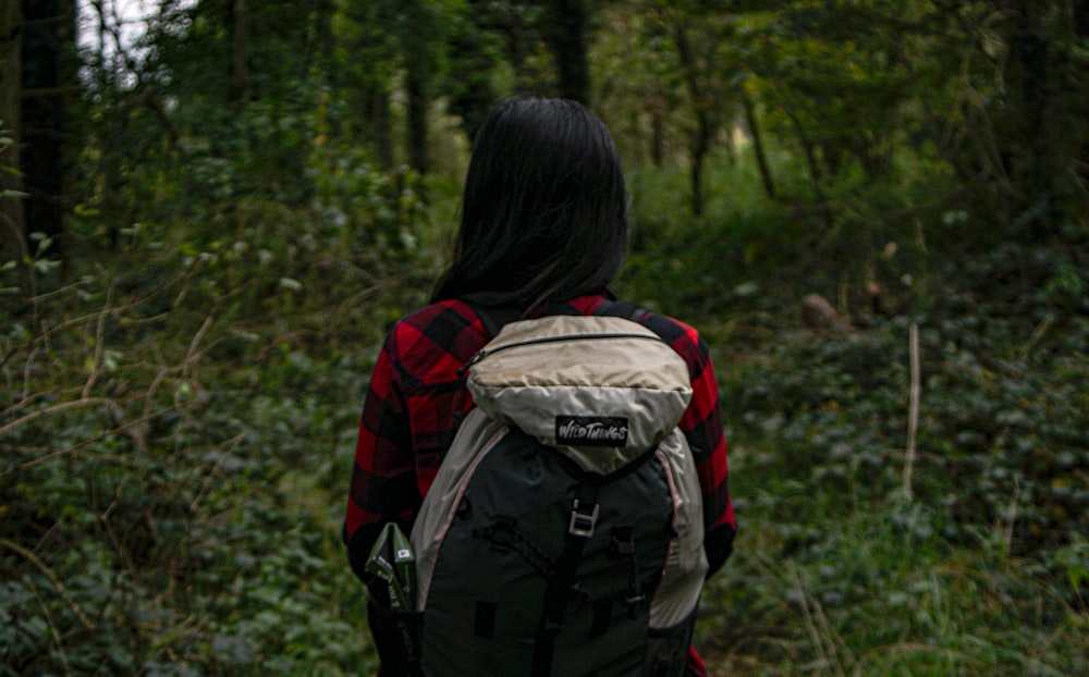 woman in red and black backpack standing on green grass field during daytime