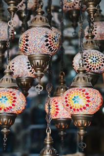 A collection of ornate hanging lamps, each featuring intricate mosaic patterns with vibrant colors. The lamps are made of stained glass and have a classic, vintage design, suspended by antique brass chains.